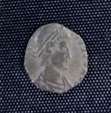 A small silver coin mostly consisting of a human head and shoulders. The shape is irregular and there is only a vestige of writing.