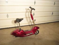 Small red scooter with a seat and handlebars. The chassis is low to the ground.