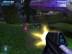 First-person view of the gameplay. In the lower-right corner of the screen, the player's weapon is shown as the player fires on small aliens in a lush outdoor environment. Indicators around the periphery of the screen display health and ammo count.