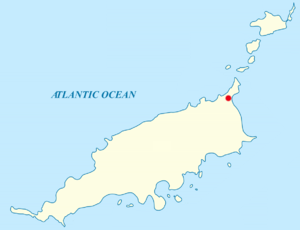 Map of an archipelago in the Atlantic Ocean. The main island is rod-shaped, oriented approximately west-southwest to east-northeast, with some irregular features in the coastline. A red label at the northeastern tip. Off the southern coast are nine smaller islands. Off the northeastern tip of the main island are five other smaller islands.