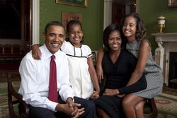 Picture of Obama, his wife, and their two daughters smiling at the camera. Obama wears a dress shirt and tie.