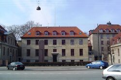 A block-shaped beige building with a sloped, red-tiled roof