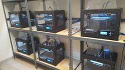 Several 3-D printers in enclosures on shelves