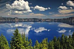 The water of Crater Lake can be seen above a forested area in the foreground.