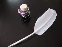 Picture of a quill and a small bottle of ink on a table.