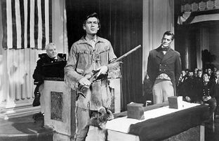 Man dressed as Davy Crockett with a rifle in his hand, alongside two men in the background