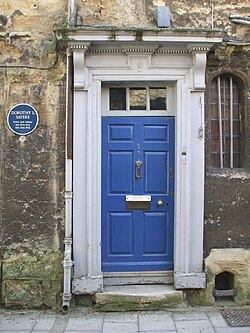 A blue door in a stone wall; a blue plaque is next to the door. This reads "Dorothy L Sayers Writer and scholar was born here 13th June 1893"