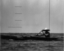 A man wearing a broad straw hat is rowing an outrigger dugout canoe has seen the periscope of the nuclear submarine USS Triton