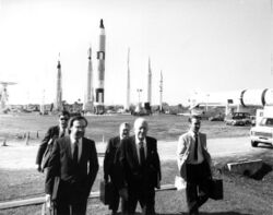 Black-and-white photo of a group of individuals at the Kennedy Space Center with the rocket garden behind them