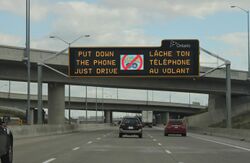 A variable-message sign over a freeway that reads "Put down the phone, just drive" with the Pokémon Go logo crossed out.