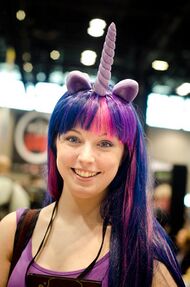 Smiling woman cosplaying Twilight Sparkle while wearing a purple and pink wig with light purple ears and a horn