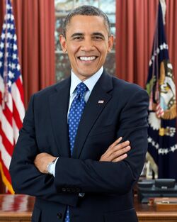 Obama standing in the Oval Office with his arms folded and smiling