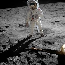 Aldrin stands on the Moon. Armstrong and the Lunar Module Eagle are reflected in his visor.