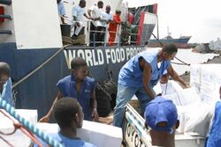 A couple of Liberian citizens (wearing blue vests that read World Food Program) unload weights of food to other citizens.