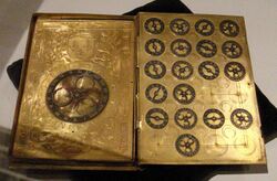 book sized metal machine with large dial left page and nineteen small dials right page