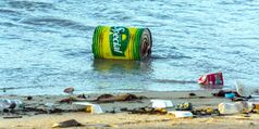 Large can floating in the ocean near other garbage on shore