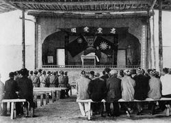 Soldiers and other sitting on benches in front of a stage