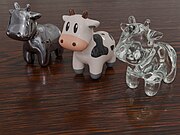 3D rendered image showing three copies of a cartoon cow. The one on the left has a metalic surface, and the one on the right uses a transparent glass material. The cow in the center appears made of glazed porcelain. The cows are standing on a wooden table. Lights and other background details from a cafe environment are reflected in the slightly glossy table and the cows.
