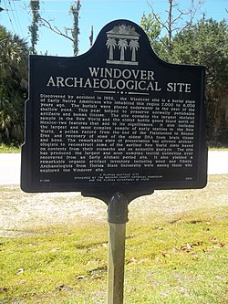 A green sign displaying the words "Windover Archaeological Site" is shown in front of a green lawn with a blue sky.