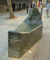 A low rectangular public monument, with a bust of Wilde's face built into one raised end, at the other at seat that one straddles to experience being in conversation with Wilde.