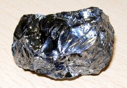 A lustrous blue grey potato-shaped lump with an irregular corrugated surface.